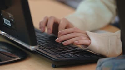 Man giving a presentation in front of a TV screen in an office with students around the table<br />
